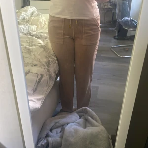 Beiga mjukisbyxor från Juicy Couture - Säljer ett par beiga mjukisbyxor från Juicy Couture i storlek XS. Byxorna har bred resår i midjan med snörning i guld, stora fickor framtill och mjukt material som känns lyxigt. Perfekta för en avslappnad och trendig look. Inget fel på dom! Köpte dom för ett tag sen men gillade inte färgen när dom kom har haft på mig dom 1 gång.