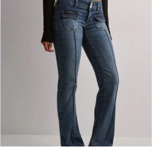 Blå bootcut jeans med fickdetaljer - Snygga blå bootcut jeans med markerade sömmar och unika fickdetaljer framtill. Jeansen har låg midja, jeansen är från Nelly och är i storlek 38 och använd få gånger 