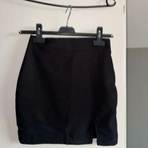 Svart kortkjol med slits - En stilren svart kortkjol med liten slits framtill. Kjolen har en enkel och klassisk design som passar till många olika outfits!