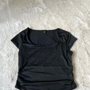 Svart topp med fyrkantig ringning från SHEIN - Säljer en svart topp från SHEIN i storlek S. Toppen har korta ärmar och en snygg fyrkantig ringning. Perfekt att styla med jeans eller kjol för en trendig look.