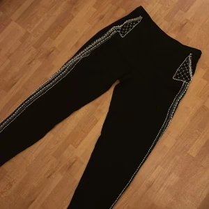 Svarta byxor med pärldetaljer - Svarta byxor med unika pärldetaljer längs sidorna och på fickorna. Byxorna har raka ben och dekorativa mönster av pärlor både upptill och vid bensluten. Perfekta för dig som vill sticka ut med en cool och trendig look.