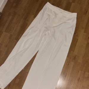 Vita kostymbyxor med hög midja - Snygga vita kostymbyxor med hög midja och raka ben. Byxorna har diskreta fickor framtill och stängs med dold dragkedja och knapp. Perfekta för en clean och stilren look.