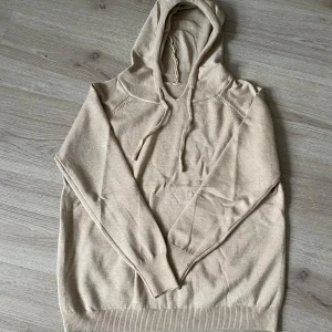 Merinoull hoodie - Säljer en stilren beige hoodie i mjukt bomullsmaterial. Tröjan har långa ärmar och en praktisk huva med dragsko. Perfekt för en avslappnad look. Den är oanvänd, säljer den för att den ej är min smak