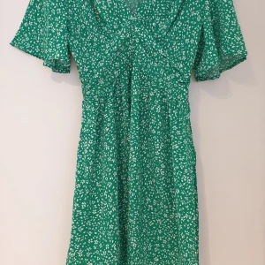 Grön blommig klänning från SHEIN - Säljer en grön kortklänning från SHEIN med vitt blommigt mönster. Klänningen har korta ärmar, v-ringad hals och markerad midja. Perfekt för vår och sommar!