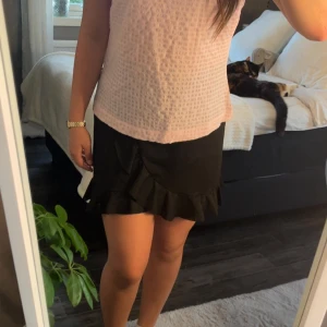 Svart volangkjol - Säljer en svart kortkjol med volangdetalj längs nederkanten och omlottkänsla framtill. Kjolen har en feminin och trendig look som passar perfekt till många olika stilar. Superenkel att matcha med både enkla och mer färgglada toppar.💞