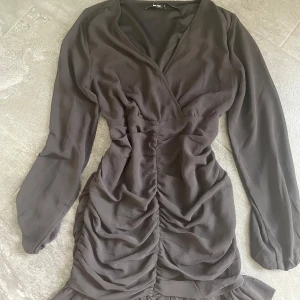 Svart omlottklänning med rynk från Bik Bok - Supersnygg svart omlottklänning från Bik Bok med långa ärmar och rynkade detaljer framtill. Klänningen har en figurnära passform och volang nertill, perfekt för dig som vill ha en stilren men trendig look.