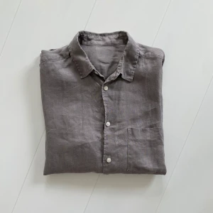 Grå linneskjorta med bröstficka - Säljer en stilren grå skjorta i linne med klassisk krage och vita knappar. Skjortan har lång ärm och en bröstficka på vänster sida. Perfekt för dig som gillar en avslappnad men snygg look.