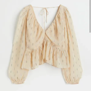 Beige blus med volang och knyt i ryggen - Söt beige blus med v-ringning, volangdetalj och knyt i ryggen där man knyter själv!. Långa, luftiga ärmar. Har kvar prislappen, utsåld. 