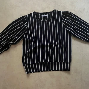 Svartvit randig tröja från D-XEL - Säljer en svart tröja med vita vertikala ränder från D-XEL. Tröjan har rund halsringning, långa puffärmar och bred mudd nertill. Perfekt för dig som gillar en stilren look med lite extra volym på ärmarna.