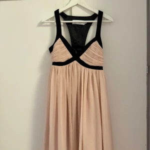Champagnefärgad klänning - Supersnygg champagnefärgad klänning från Lipsy London med svarta kontrastdetaljer och breda axelband. Klänningen har v-ringning, markerad midja och plisserad kjol. Midi längd. Ej genomskinlig och har ett lager under. Pris odiskuterbart!!!