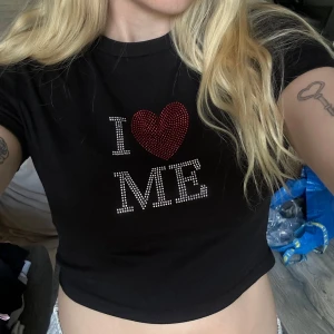Svart croppad t-shirt med strasstext - Svart croppad t-shirt med texten 'I ♥ ME' i glittriga stenar. Hjärtat är rött och resten av texten är i vita stenar. Perfekt statement-plagg för dig som vill sticka ut 🩷