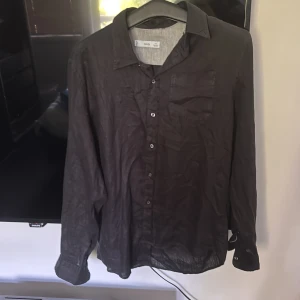 Svart linneskjorta från MNG - Säljer en svart långärmad skjorta från MNG i linnematerial. Skjortan har klassisk krage, knäppning framtill och en bröstficka. Passformen är slim och materialet känns svalt och luftigt.