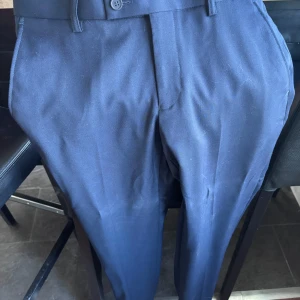 Mörkblå kostymbyxor från Dressmann - Säljer ett par mörkblå kostymbyxor från Dressmann i slim fit-modell. Byxorna har klassisk design med knäppning fram, bälteshällor och fickor bak med knapp. Perfekta för en stilren look. Har använt dom en gång. Kostar 800kr nypris.