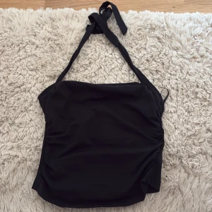 Svart omlott tubtopp med knytband - Säljer en svart tubtopp med omlott-design och knytband upptill. Toppen har en stilren look och är perfekt för varma dagar eller som ett lager under en skjorta. Materialet känns mjukt och följsamt.