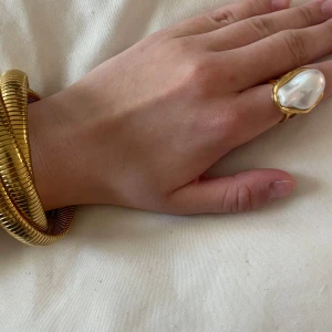 Guldfärgad ring med stor pärla - Aldrig använd! Trendig guldfärgad ring med en stor vit pärla från Scandivv. Ringen har öppen baksida, så den är justerbar, och en elegant, modern design som sticker ut. Perfekt accessoar för att lyfta din outfit.