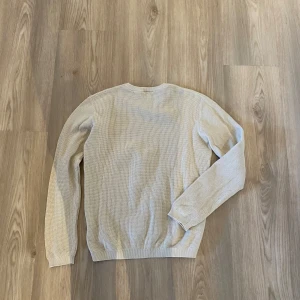 Beige stickad tröja från D.M.D - Säljer en beige stickad tröja från D.M.D. Tröjan har rund halsringning och långa ärmar. Den är enkel och stilren med diskret struktur i materialet, perfekt för en avslappnad look.