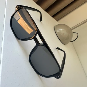 Svarta solglasögon med bred båge - Snygga svarta solglasögon med bred, markerad båge och stora, mörka glas. Klassisk design med en modern touch, perfekt för dig som vill sticka ut. Passar de flesta ansiktsformer och ger en cool look.
