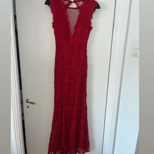 Röd lång spetsklänning med v-ringning - Säljer en elegant röd långklänning med djup v-ringning och spetsdetaljer. Klänningen är ärmlös och har en snygg öppen rygg samt dragkedja bak. Perfekt för bal eller festliga tillfällen. Figurnära passform och vackert spetsmönster. Storlek S/36 men stretchiga tyg!🥰🥰kan skicka på direkten (köpt i Spanien så jag vet inte märket)