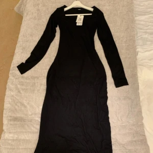 Svart långklänning från Bik Bok - Svart långklänning från Bik Bok i figurnära modell. Klänningen har långa ärmar och en rundad halsringning. Perfekt för dig som gillar en stilren och enkel look. Materialet känns mjukt och stretchigt.