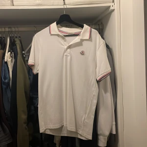 Vit pikétröja från Moncler - Säljer en klassisk vit pikétröja från Moncler med röd och marinblå rand på krage och ärmslut. Passar storlek M. Skriv vid funderingar! Våga skicka prisförslag!