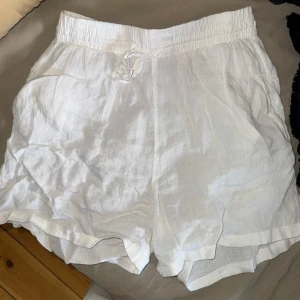 Vita linneshorts med dragsko - Säljer ett par vita shorts i linne med elastisk midja och snörning framtill. De har en avslappnad passform och sidfickor, perfekta för varma dagar och nu inför sommaren. Dem är lite skrynkliga men går lätt att lösa med strykjärn eller likande.