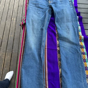 Blå jeans från Nudie Jeans - Säljer ett par klassiska blå jeans från Nudie Jeans med orangea sömmar och fem fickor. Jeansen har normal passform och raka ben, perfekt för en avslappnad stil. Midjan är normal och materialet är slitstarkt denim. OANVÄNDA