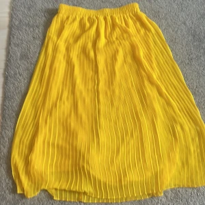 Gul plisserad kjol från Monki - Säljer en solgul plisserad kjol från Monki med resår i midjan. Kjolen är lång och har en luftig känsla, perfekt för att liva upp din outfit. Superfin färg och snyggt fall!