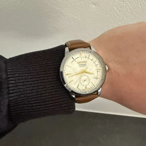 Seiko Presage mod - Seiko Presage Mod med en klassisk vit urtavla och ett elegant läderfärgat armband. En perfekt kombination av japansk hantverkskvalitet och unik design som gör sig lika bra till vardags som till mer uppklädda tillfällen. Klockan har ett automatiskt urverk som håller tiden bra.