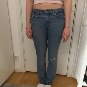 Blå Levis 501 jeans med bootcut ben - Klassiska blå Levis 501 jeans med normal passform och bootcut ben. Byxorna har fem fickor, knappgylf och en liten slitning på ena benet. De är mycket stretchiga och perfekta för en avslappnad stil.