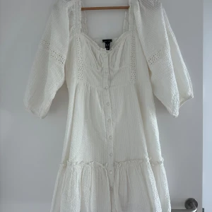 Vit klänning med puffärmar och knappar - Superfin vit klänning med puffiga trekvartsärmar och knappar framtill. Klänningen har volangdetaljer och en lätt strukturerad yta. Perfekt för sommarens alla tillfällen! Aldrig använd.