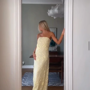 Ljusgul axelbandslös långklänning med blommigt mönster - Säljer en elegant ljusgul axelbandslös långklänning med blommigt mönster. Klänningen har en rak, smickrande passform. Ny, prislapp kvar! Kan skicka samma dag som köp sålänge det inte är sent på kvällen 💕💕💕 SÄLJER FÖR 900 kr idag!!