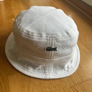Lacoste Buckethat - Fräsch, knappt använd buckethat från Lacoste. Färg: Vit, Storlek:S