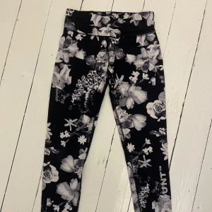 Svarta träningstights med blommigt mönster - Snygga svarta tights med vita och gråa blommor från Swedemount. Hög midja och tight passform, perfekta för träning. Mjukt och stretchigt material som sitter skönt på kroppen.