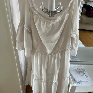 Vit volangklänning med v-ringning - Säljer en romantisk vit klänning med v-ringning och volangdetaljer. Klänningen har trekvartsärmar med lätt puff och är sydd i ett mjukt, flowy material. Perfekt för sommarens alla tillfällen.