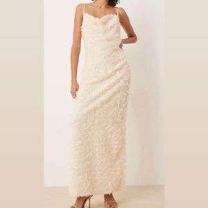 Cremefärgad långklänning med fjäderdetaljer från Vila - Säljer en helt ny elegant långklänning från Vila i en cremefärg med tunna axelband och fjäderliknande struktur i tyget. Dragkedja baktil, slits bak, halsringning, normal passform. Köpte fel storlek, hann ej lämna tillbaka. Prislapp på! 