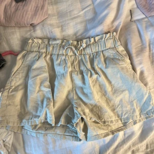 Beige shorts med volangkant från Lindex - Säljer ett par ljusbeige shorts från Lindex med volangkant upptill och resår i midjan. Shortsen har en lös passform och är perfekta för varma dagar. Tillverkade i ett mjukt och svalt material. linneshorts som passar väldigt fint till en shorts tillexempel. otroligt sköna