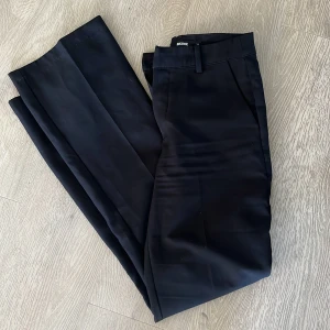 Svarta kostymbyxor från Bik Bok - Stilrena svarta kostymbyxor från Bik Bok med klassisk rak passform och pressveck. Byxorna har hällor för bälte och diskreta fickor. Perfekta för en dressad look och passar till många olika tillfällen.