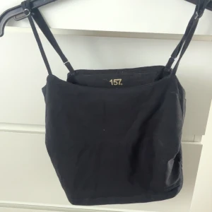 Svart linnetopp från 157 - En enkel svart linnetopp från 157 med smala axelband. Tillverkad i bomull och elastan för en bekväm passform. Perfekt att matcha med jeans eller kjol.