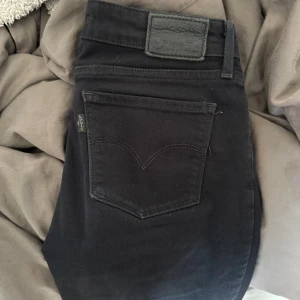 Svarta jeansbyxor från Levi's - Svarta jeansbyxor från Levi's med klassisk femficksdesign och svarta detaljer. Byxorna har normal passform och dragkedja framtill. Perfekta till många olika outfits. Bootcut