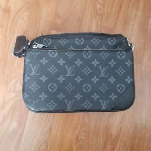 Louis Vuitton axelväska med monogram - Säljer en snygg axelväska från Louis Vuitton i svart med klassiskt monogrammönster. Väskan har silverfärgade detaljer, justerbar axelrem och dragkedja. Tillverkad i skinn och polyester, perfekt för att bära dina viktigaste saker.