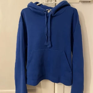 Blå hoodie med huva och magficka - Säljer en enkel blå hoodie i storlek M - med huva samt en stor magficka framtill. Tröjan har långa ärmar och är i mjukt & tjockt material, perfekt för en avslappnad stil.