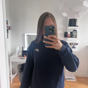 Mörkblå sweatshirt från Nike - Säljer en mörkblå sweatshirt från Nike med klassisk vit logga broderad på bröstet. Tröjan har rund halsringning och långa ärmar. Perfekt för en avslappnad och sportig stil.