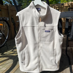 Vit/beige  fleeceväst från Patagonia - Säljer en beige fleeceväst från Patagonia med dragkedja. Västen har en bröstficka med logotyp och två sidofickor. enkel att matcha med olika outfits. Snygg till sommaren. Använd i 2 månader så nästan helt ny. Skick som ny, storlek s 