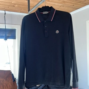 Svart pikétröja från Moncler - Snygg svart pikétröja från Moncler med klassisk krage och knappar framtill. Tröjan har långa ärmar och en stilren logga på bröstet. Perfekt för en stilren outfit. Använd 3-4 gånger👌🏽vid minsta fundering eller fråga så är det bara att höra av sig.