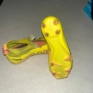 Gula fotbollsskor från Nike - Säljer ett par gula Nike Air Zoom fotbollsskor med en unik design. Skorna har en elastisk rem över vristen och en greppvänlig sula med dobbar för optimalt fäste på planen. Perfekta för den som vill sticka ut på fotbollsplanen!