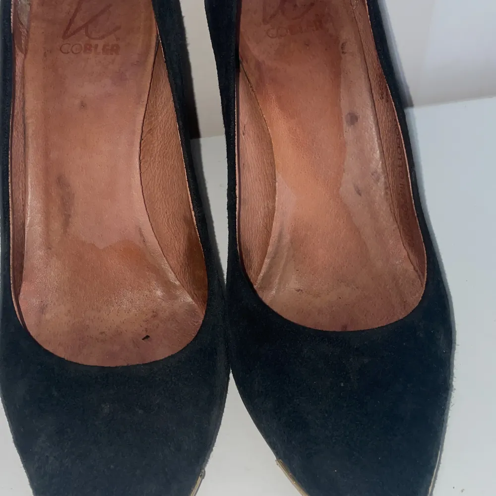 Eleganta svarta pumps i mocka med spetsig tå och klack( 9 cm). Skorna har en stilren design med en subtil gulddetalj vid tån. Perfekta för en chic look.. Kengät.