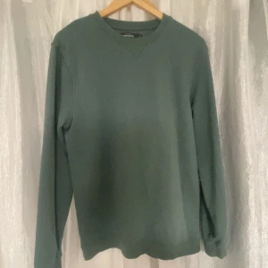 Grön tröja från Dressmann - Säljer en stilren grön tröja från Dressmann i storlek M. Tröjan har en klassisk rund hals och långa ärmar, perfekt för en avslappnad look. Passar bra till både jeans och chinos.