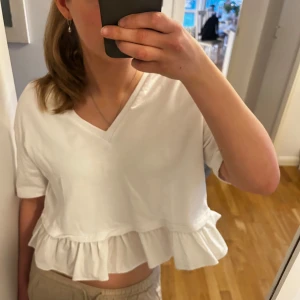 Vit kortärmad blus med volang - Säljer en söt vit blus/tröja med korta ärmar och v-ringning från Zara💕. Blusen har en volangdetalj nertill och är lite kortare i modellen Perfekt till ett par jeans eller en kjol. Säljer då den inte kommer till användning längre och blivit för kort för mig tyvärr. Är runt 1.70🩷 pris kan diskuteras då jag bara vill bli av med tröjan! 