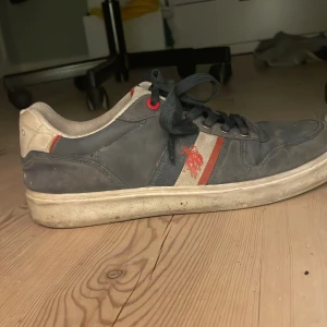 Blå sneakers från U.S. Polo Assn. - Snygga blå sneakers från U.S. Polo Assn. med vita och röda detaljer. Skorna har snörning och en vit sula. Perfekta för en avslappnad stil. Kommer tvätta dom innan jag fraktar 
