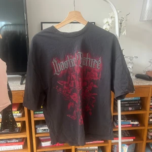 Svart t-shirt från Bershka - Säljer en svart t-shirt från Bershka med ett coolt rött tryck på framsidan och rhinestones. T-shirten har en normal passform och korta ärmar. Perfekt för en avslappnad stil.